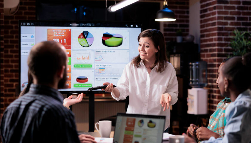 Une femme qui pdiscue avec un homme devant un écran avec des diagrammes